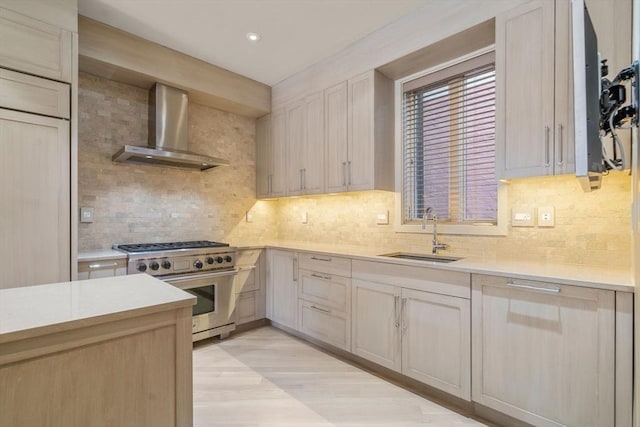 kitchen featuring a sink, high end stainless steel range, wall chimney exhaust hood, decorative backsplash, and light countertops