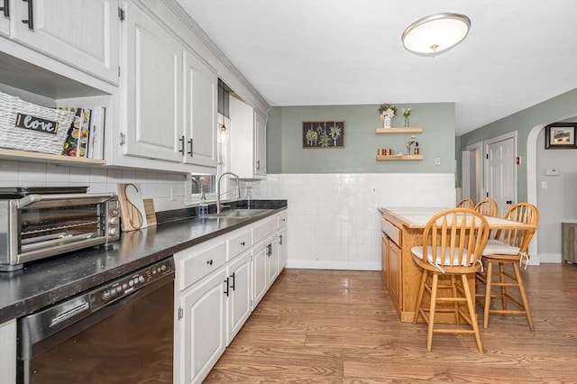 kitchen with black dishwasher, a breakfast bar area, sink, white cabinets, and light hardwood / wood-style flooring