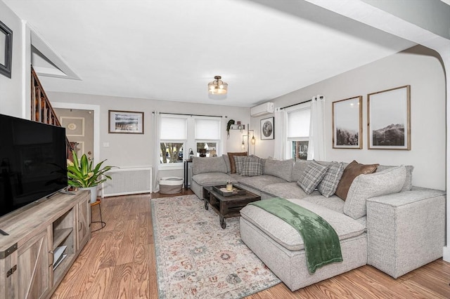 living room featuring an AC wall unit, radiator, a wealth of natural light, and light hardwood / wood-style flooring