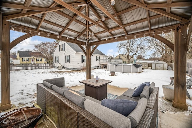 snow covered patio with a fenced in pool, a gazebo, an outdoor living space with a fire pit, and a storage unit