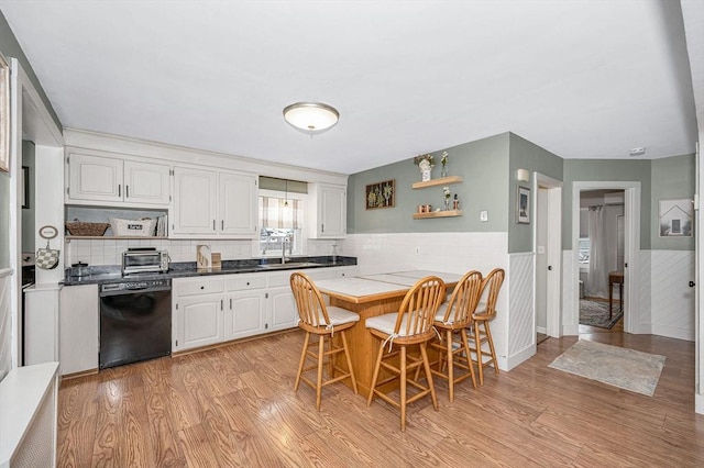 kitchen with white cabinetry, dishwasher, sink, a kitchen breakfast bar, and light hardwood / wood-style floors