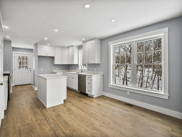 kitchen with a kitchen island, appliances with stainless steel finishes, white cabinetry, sink, and light hardwood / wood-style floors