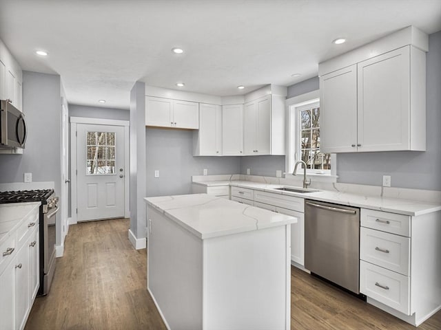 kitchen featuring sink, light stone counters, appliances with stainless steel finishes, a kitchen island, and white cabinets