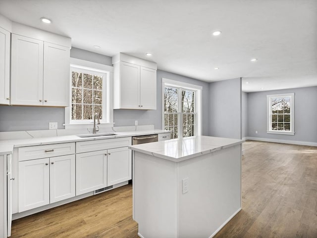 kitchen with white cabinetry, sink, a center island, stainless steel dishwasher, and light wood-type flooring