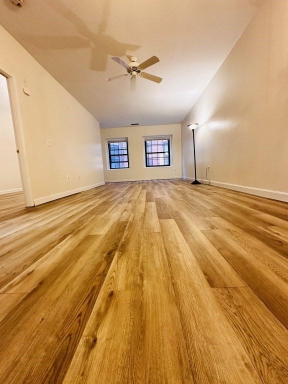 unfurnished living room featuring a ceiling fan, baseboards, vaulted ceiling, and light wood finished floors