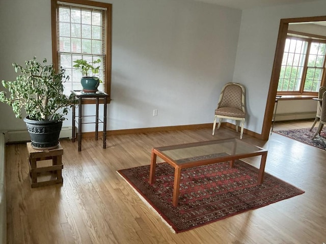 living area featuring baseboard heating, baseboards, a baseboard heating unit, and wood finished floors
