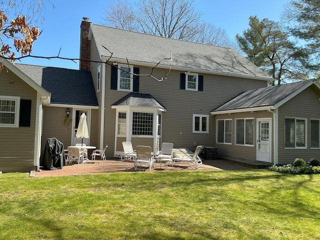 back of property featuring roof with shingles, a patio, a chimney, and a yard