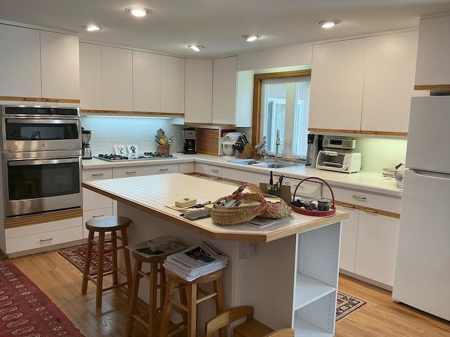 kitchen with stainless steel double oven, gas cooktop, a breakfast bar, a sink, and freestanding refrigerator