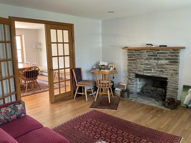 living area with a stone fireplace, french doors, and wood finished floors