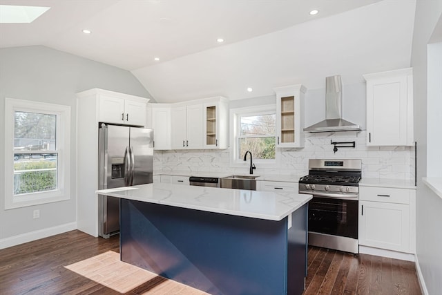 kitchen with lofted ceiling with skylight, wall chimney exhaust hood, a kitchen island, dark hardwood / wood-style flooring, and stainless steel appliances