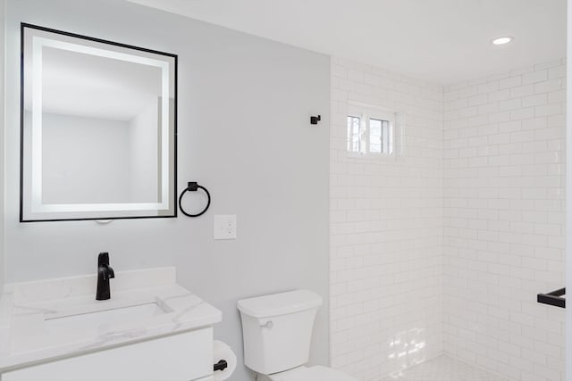 bathroom with a tile shower, vanity, and toilet