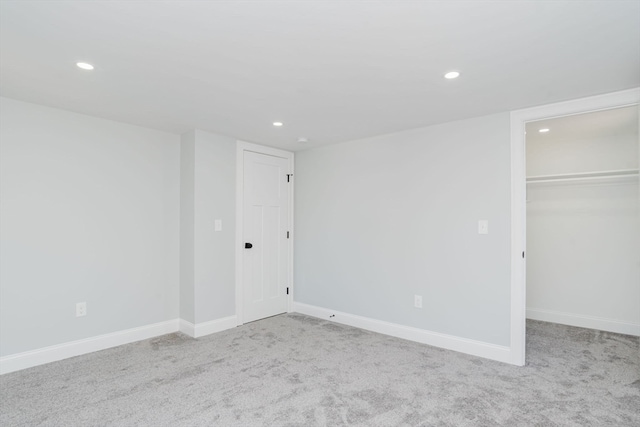 unfurnished bedroom featuring a walk in closet, a closet, and light colored carpet