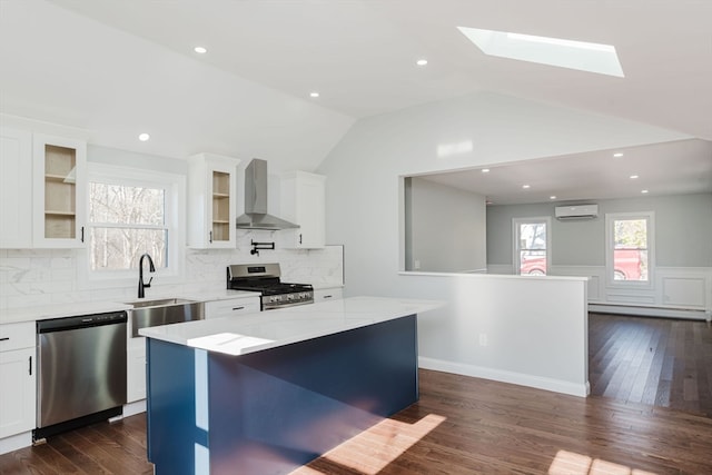 kitchen with a center island, vaulted ceiling with skylight, wall chimney exhaust hood, white cabinetry, and stainless steel appliances