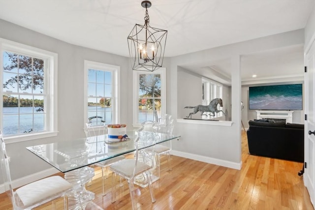 dining room featuring light wood finished floors, a water view, a chandelier, and baseboards