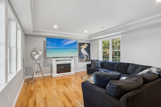 living area featuring a fireplace with raised hearth, light wood-style flooring, a raised ceiling, and baseboards