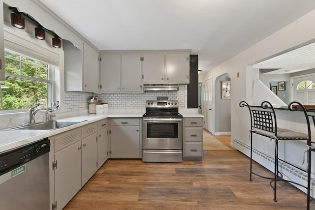 1026 Chandler St, Tewksbury, MA 01876 - kitchen featuring appliances with stainless steel finishes, under cabinet range hood, gray cabinetry, backsplash, and dark wood-style floors