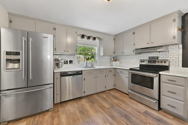 1026 Chandler St, Tewksbury, MA 01876 - kitchen with appliances with stainless steel finishes, under cabinet range hood, light wood-style flooring, tasteful backsplash, and light countertops