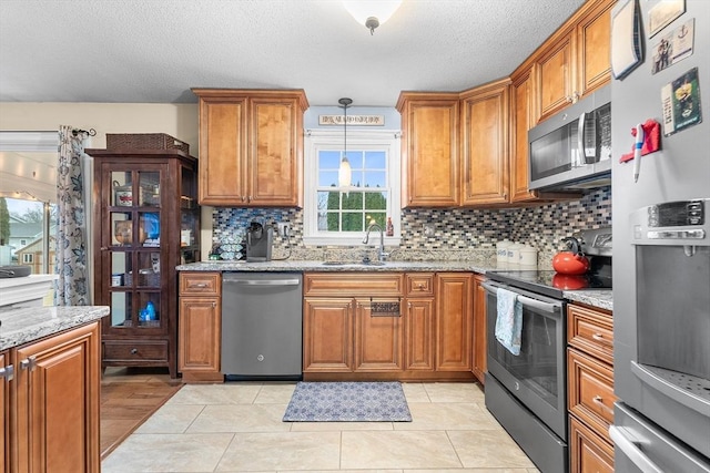 kitchen with light stone countertops, sink, stainless steel appliances, and decorative light fixtures