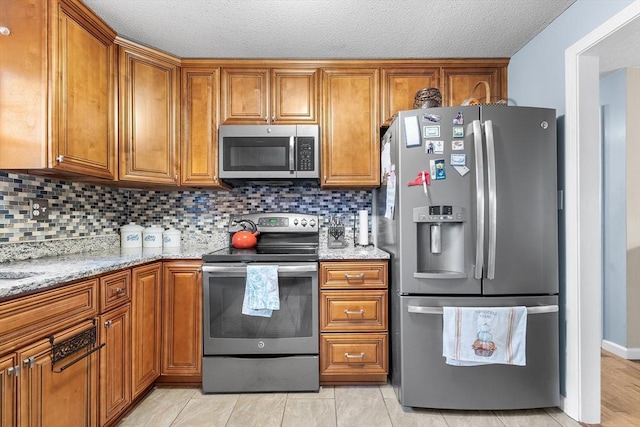 kitchen featuring backsplash, light stone countertops, stainless steel appliances, and a textured ceiling