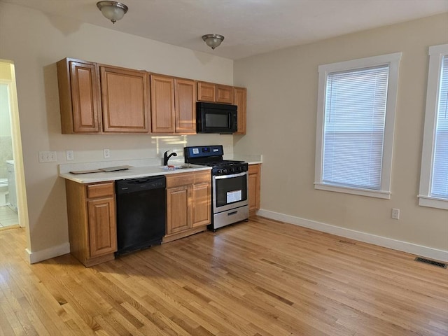 kitchen with sink, a wealth of natural light, black appliances, and light hardwood / wood-style flooring