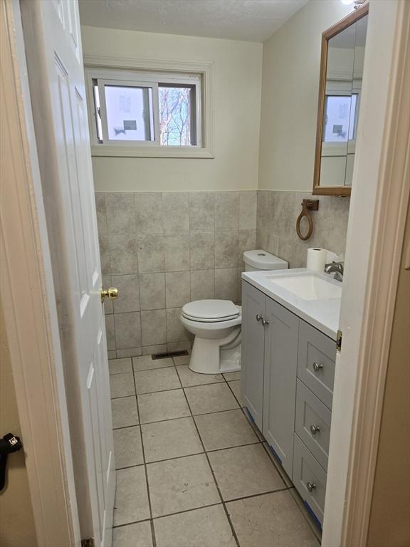 bathroom featuring toilet, vanity, tile patterned floors, and tile walls