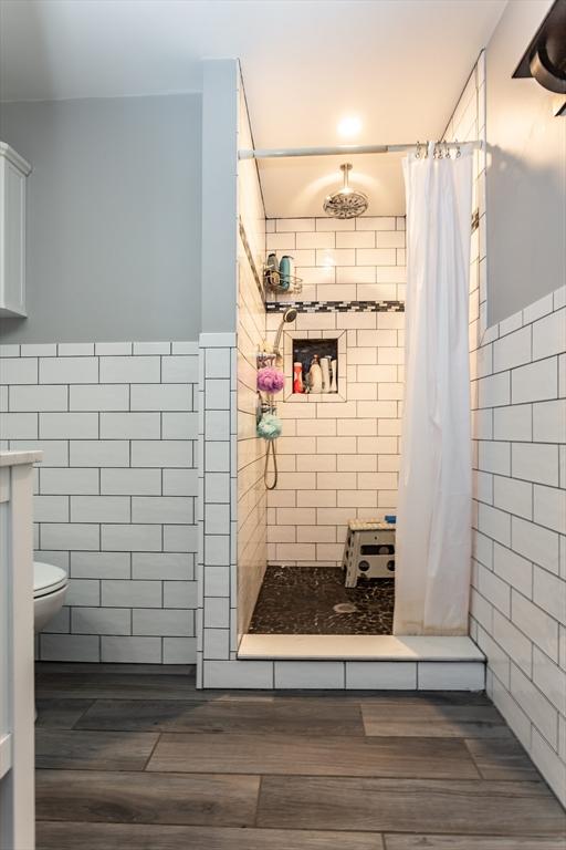 bathroom with toilet, tile walls, hardwood / wood-style flooring, and walk in shower