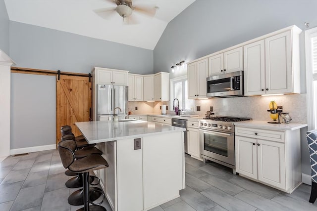 kitchen with a barn door, a kitchen island, sink, a breakfast bar area, and stainless steel appliances