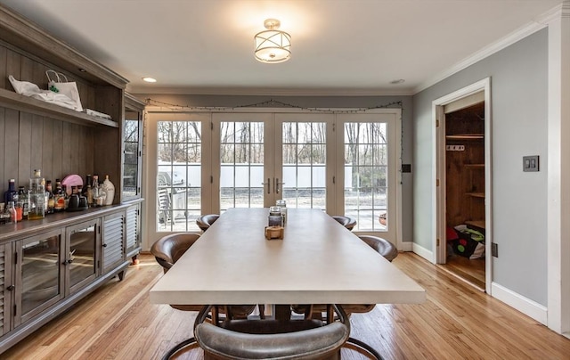 dining room featuring light wood-type flooring, a wealth of natural light, ornamental molding, and french doors