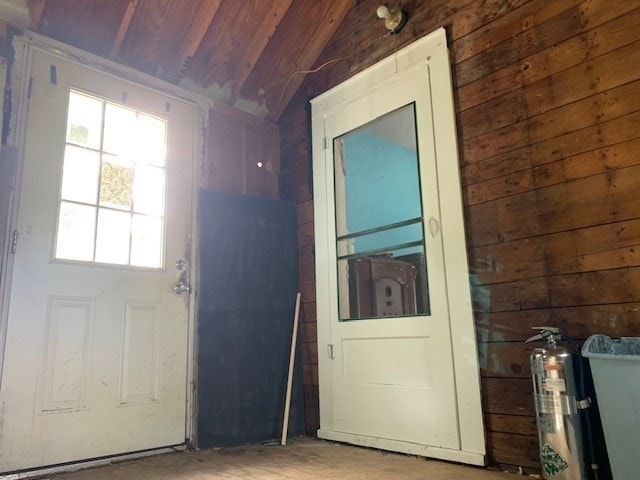 doorway to outside with vaulted ceiling, a healthy amount of sunlight, and wood walls