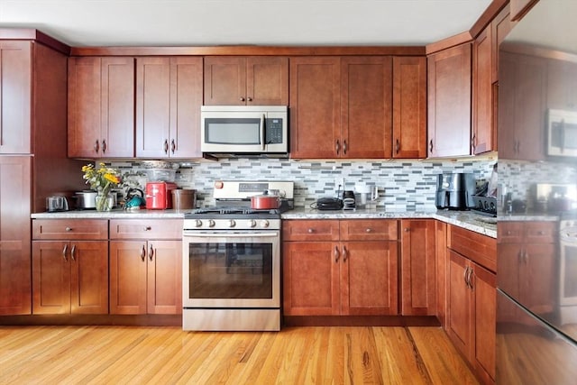 kitchen with light wood-type flooring, brown cabinets, appliances with stainless steel finishes, decorative backsplash, and light stone countertops