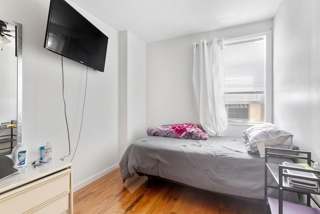 bedroom with cooling unit, baseboards, and light wood-style flooring