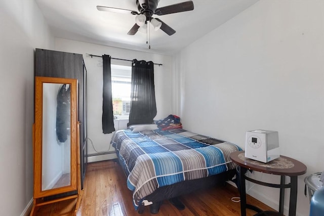 bedroom with a baseboard radiator, wood finished floors, and a ceiling fan