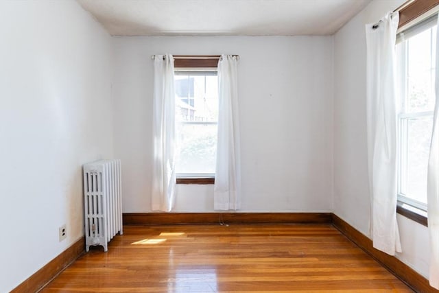 empty room with light wood-style floors, radiator, and baseboards