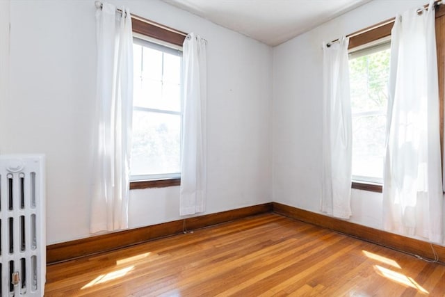 unfurnished room with baseboards, light wood-style flooring, and radiator heating unit