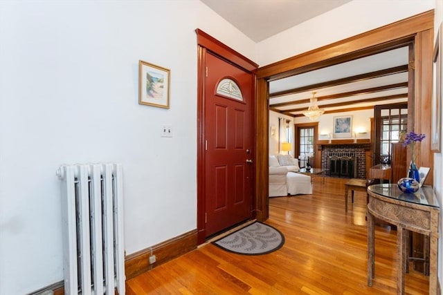 entryway with an inviting chandelier, a brick fireplace, wood finished floors, baseboards, and radiator heating unit