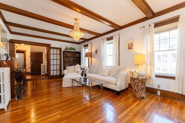 living area with crown molding, beam ceiling, a chandelier, baseboards, and wood finished floors