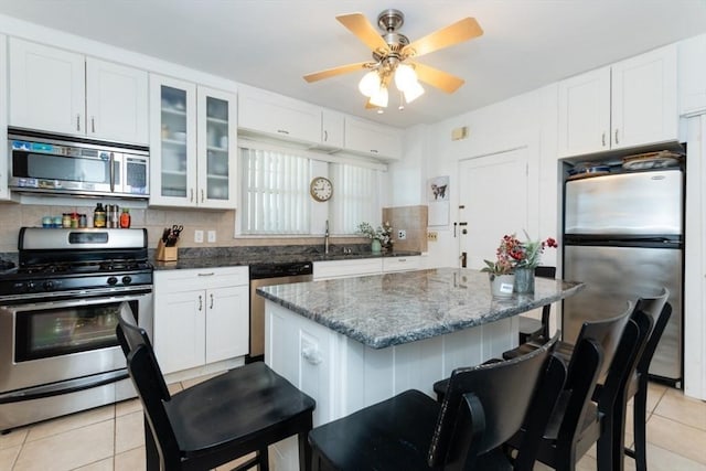 kitchen featuring white cabinets, a breakfast bar, stainless steel appliances, light tile patterned floors, and glass insert cabinets