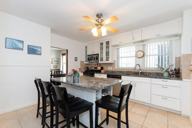 kitchen featuring light tile patterned flooring, a kitchen bar, a sink, appliances with stainless steel finishes, and backsplash