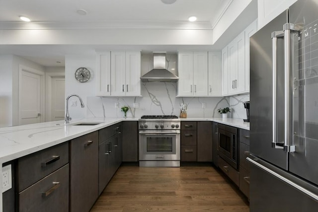 kitchen featuring high end appliances, sink, white cabinets, and wall chimney range hood