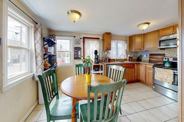 kitchen with stainless steel appliances, tasteful backsplash, light tile patterned flooring, a sink, and baseboards