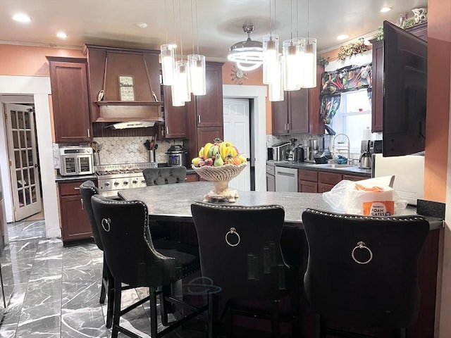 kitchen featuring sink, a breakfast bar area, backsplash, hanging light fixtures, and custom range hood