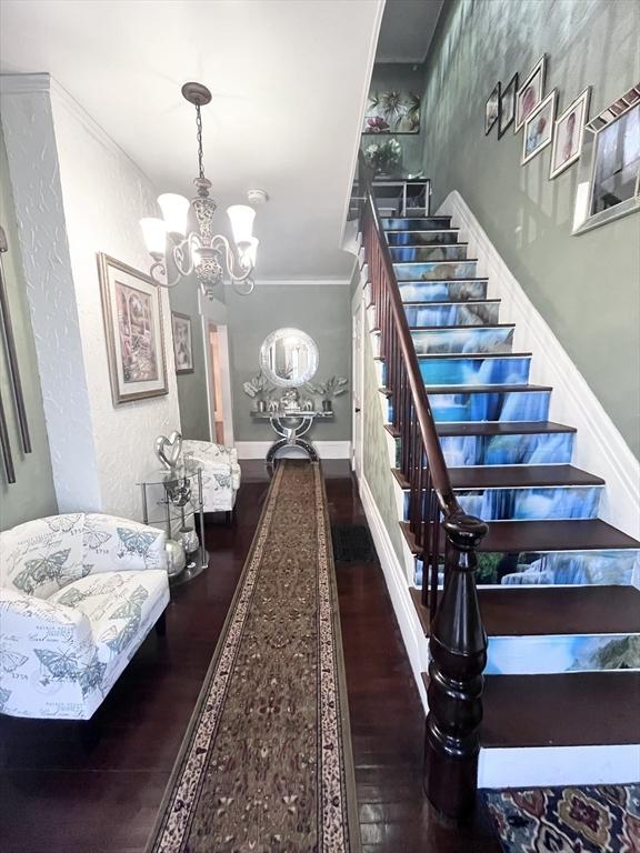 stairs featuring a notable chandelier, wood-type flooring, and ornamental molding