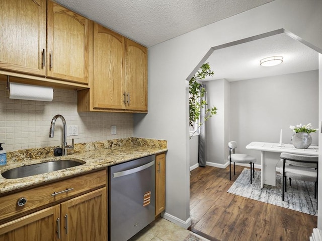 kitchen with decorative backsplash, light wood-style flooring, light stone counters, stainless steel dishwasher, and a sink