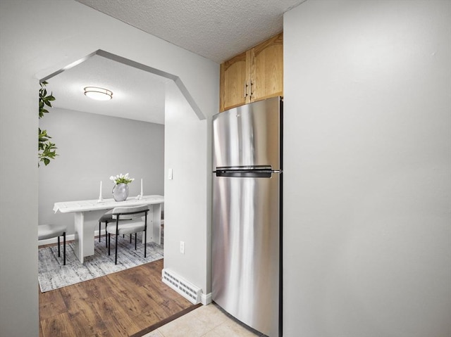 kitchen with light wood finished floors, visible vents, freestanding refrigerator, a textured ceiling, and light brown cabinetry