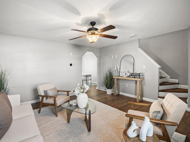 living area with baseboards, arched walkways, a ceiling fan, wood finished floors, and stairs