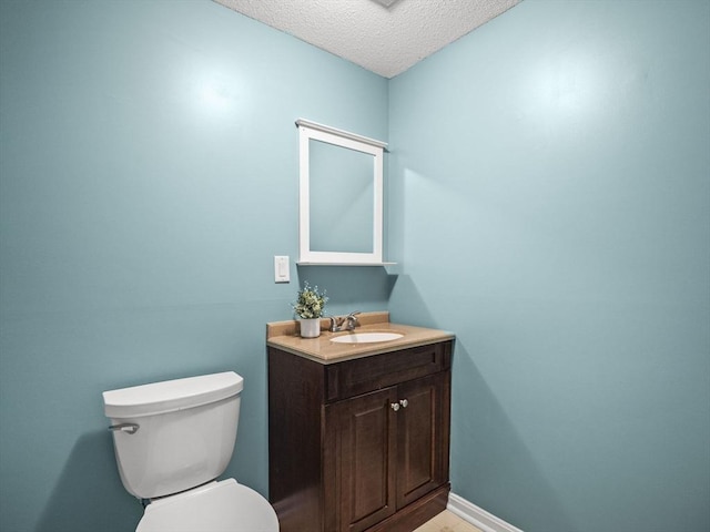 bathroom featuring a textured ceiling, vanity, toilet, and baseboards