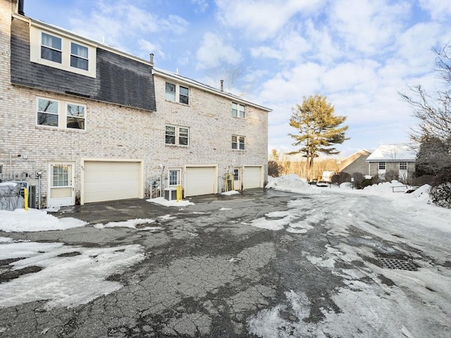 exterior space with brick siding, mansard roof, a shingled roof, a garage, and driveway