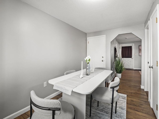 dining room featuring arched walkways, dark wood finished floors, a textured ceiling, and baseboards