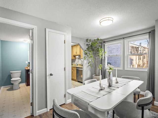 dining room with a textured ceiling, baseboards, and light wood finished floors