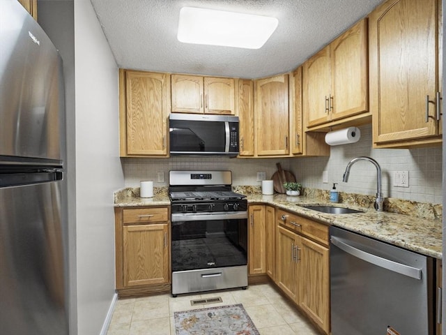 kitchen featuring light stone counters, light tile patterned floors, tasteful backsplash, appliances with stainless steel finishes, and a sink